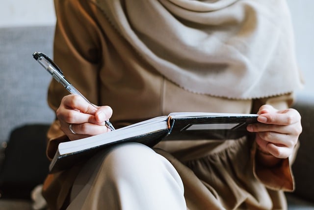 Female wearing a shawl, writing in a hard covered note book