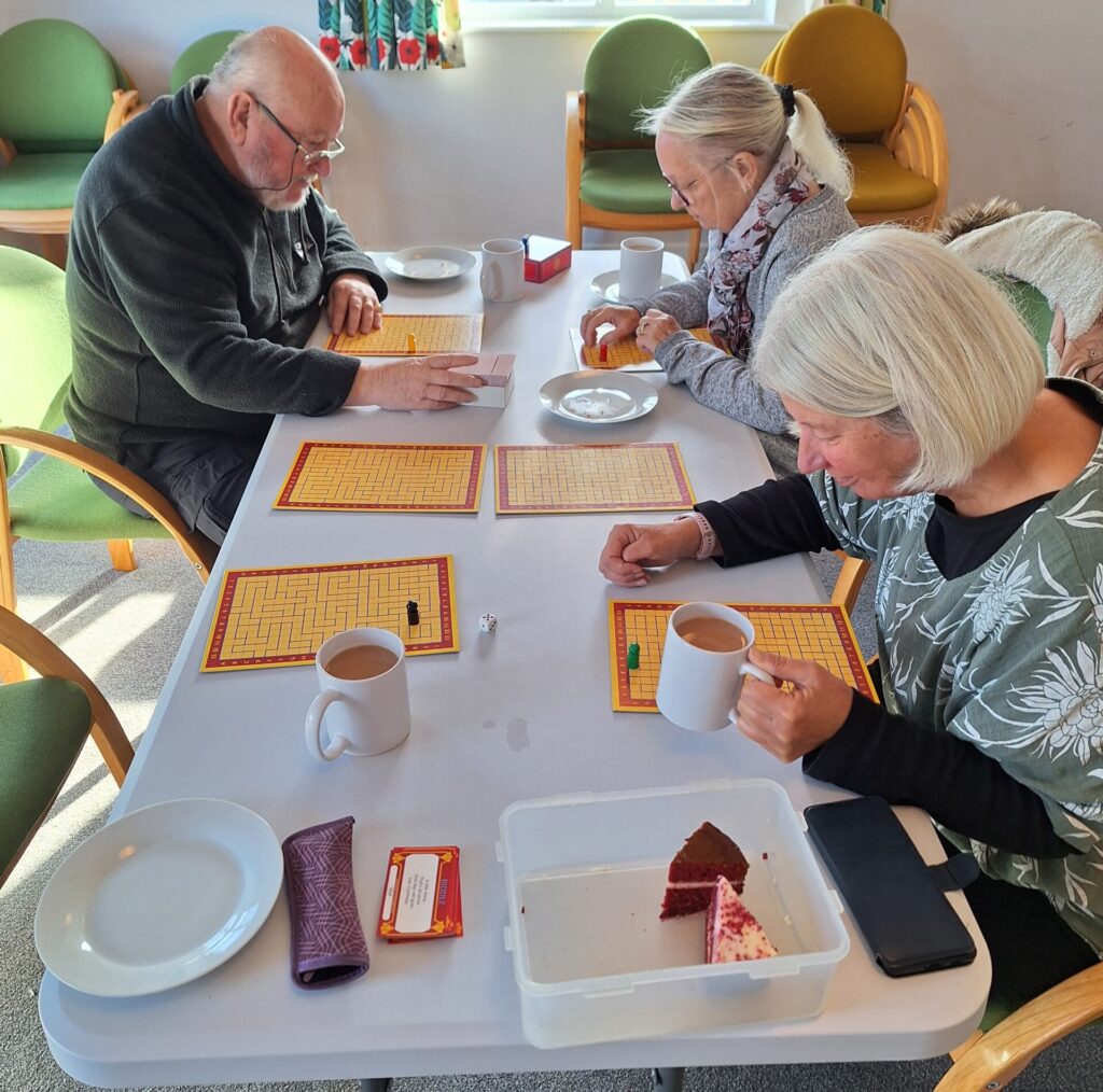 A group of 3 people sat around a table drinking a hot drink whilst completing a puzzle