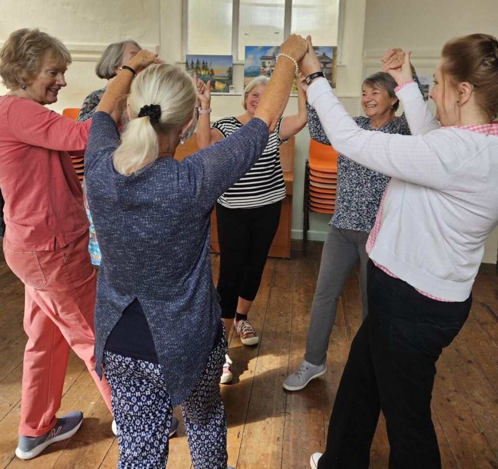 A image of 6 people with hands linked in the air, formed in a circle dancing