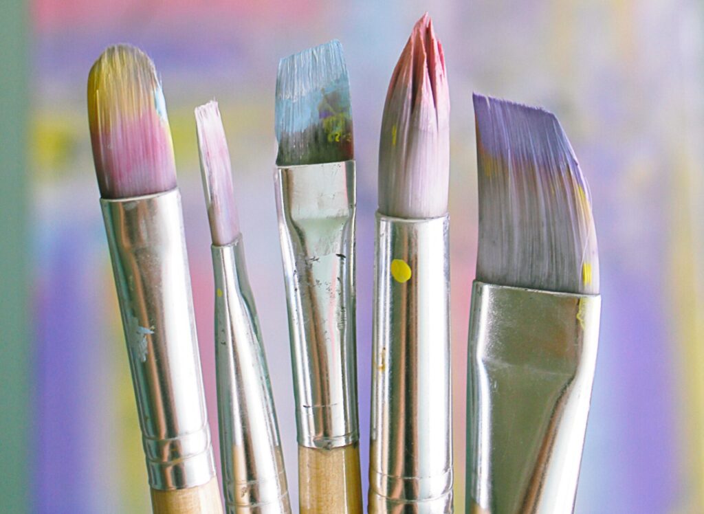 The tops of 5 paint brushes, that are used for detailed art work, each with a different shade of paint