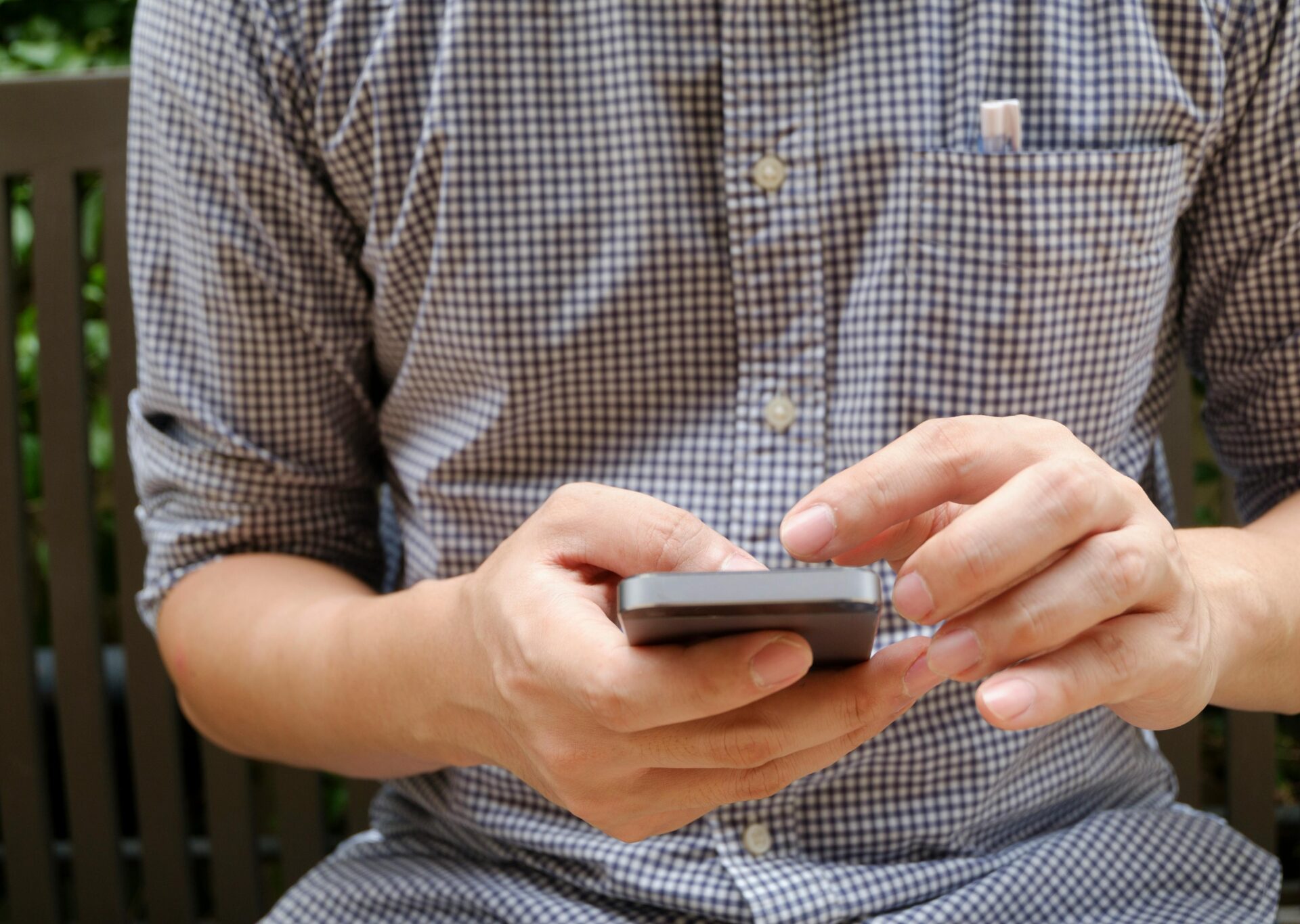 A man sitting down using 2 hands to use mobile phone