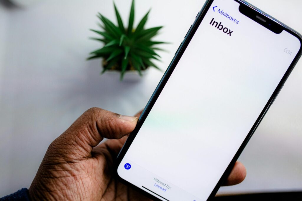 A hand holding a mobile phone displaying an empty email inbox 